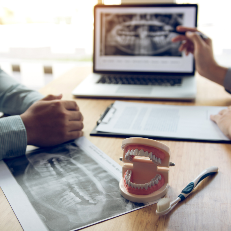 photo of a desk with a tooth model, computer monitor, and dr and patient hands